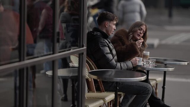A couple enjoys coffee at a in Paris France The man and woman are sitting at an outdoor table stirring their drinks. This is a romantic date in Europe showcasing a lifestyle scene.