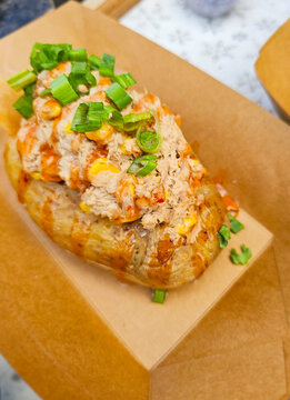 Baked potato kumpir with chicken, corn, and spicy sauce in a take-away box