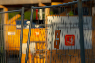 close up fence arrow with container backdrop, contractor checking route while equipment rests, warm sunset light highlights safety labels, temporary fencing marking work perimeter