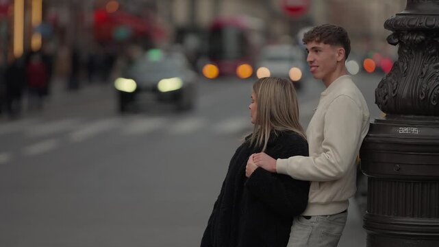 A romantic couple stands by a lamp post on a bridge in Paris France looking out at the city street Cars and people pass by in the blurred background The scene captures a moment of affection and togeth