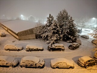 Winter night in the city with snow-covered cars, sidewalks and roads. Snow disaster in a housing estate in Eastern Europe.