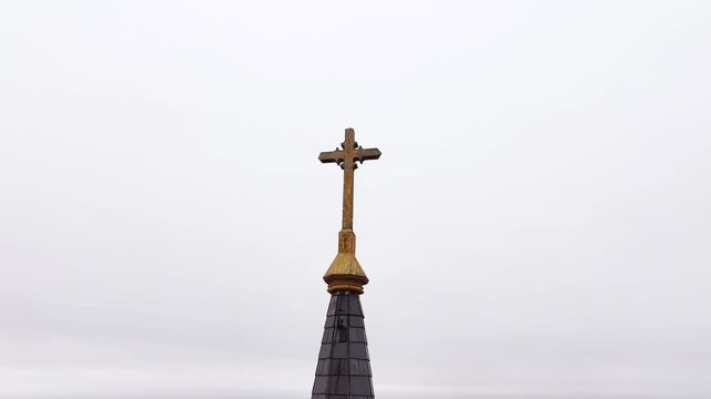 360 looping around a brass crucifix cross on top of a church steeple with shingles on an overcast day with no clouds symbolizing religion and God.