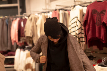 Checking coat fit and mobility, Attempting on jacket while assessing arm movement and comfort levels, Trying on outerwear and evaluating sleeve length alongside casual clothing displays