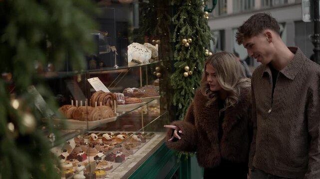A young couple window shopping at a patisserie in Paris during the Christmas season The lovers are admiring the pastries and desserts in the bakery shop display case.