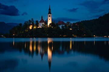 The stunning Pilgrimage Church of Mary the Queen rests on a small island in Lake Bled, Slovenia, during blue hour.
