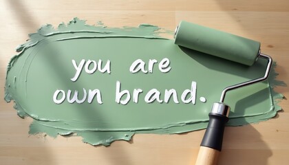 Paint roller applies green color with phrase you are own brand. Message conveys personal identity, creativity, and self expression on wood. Motivational concept inspires individuality.