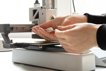 A woman's hands unscrew a screw on a 3D printer with a hex key, on a white background. The topic is 3D printer maintenance and repair