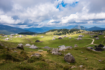 A wide panoramic view of a traditional shepherd village with unique wooden huts scattered across green rolling hills under a dramatic sky in Velika Planina, Slovenia.