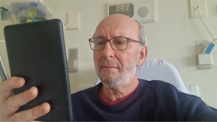 Senior man patient reading ebook in hospital room