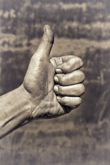 Industrial worker hand showing thumbs up agreement gesture after completed work. Sephia effect.