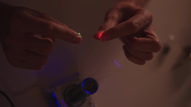 Hands conducting tesla coil experiment, high-voltage arcs wirelessly lighting leds, demonstrating electromagnetic induction, energy transfer and physics in dark lab setting, close-up, slow motion.
