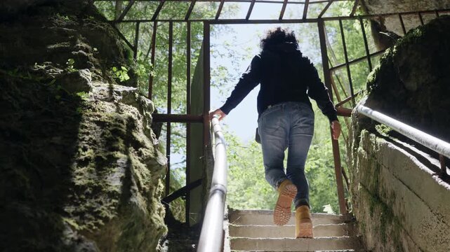 Woman climb on stairs visiting mystic view underground cave Devil's Throat (Dyavolsko garlo ) cave in the Rhodope Mountains, abundantly overgrown with deciduous and evergreen forest 