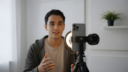 Young man recording video content with smartphone and camera in bright room