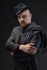 Character portrait of man blending noir aesthetics with ethnic elements in his suit and hat choice, captured in professional studio on gray backdrop.