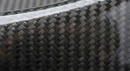 Close-up of a carbon fiber composite material with a glossy finish, showing the intricate woven pattern and texture.
