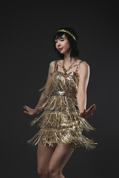 Art Deco beauty in golden flapper dress with pendant necklace and headband, Dancing
