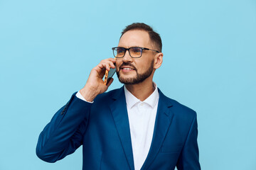 A professional man in a business suit stands against a solid blue background, exuding confidence and focus while on a mobile call.
