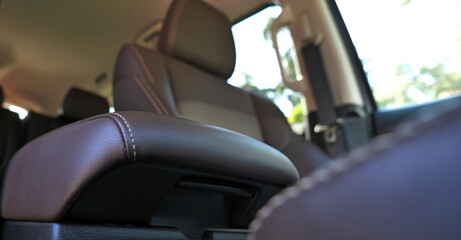 A bottom view of a brown leather armrest against a blurred driver's seat in a business class car
