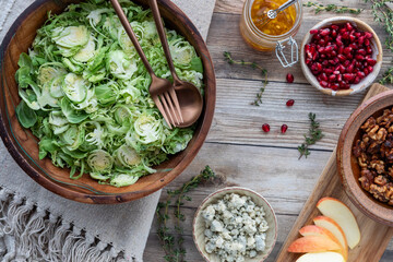 Shaved Brussels Sprouts in a wooden bowl with salad ingredients all around.