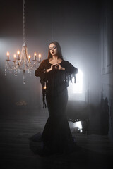 A gothic femme fatale with long straight hair and dark makeup wears a black godet skirt dress with corset, posed in a luxurious dimly lit gothic interior.