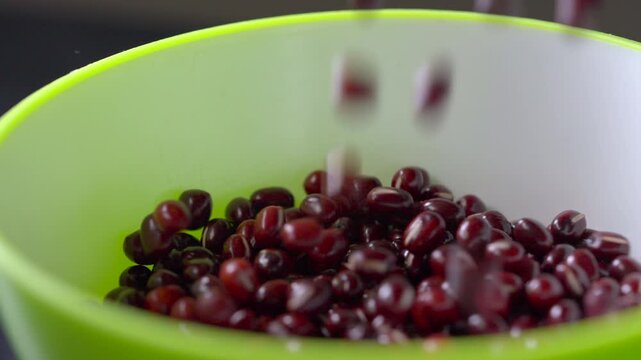 Dried red beans falling slowly into a plastic neon green and white bowl