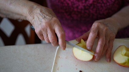 Elderly woman slices an apple while talking on a video call in the kitchen, preparing a tasty fruit salad to share with family