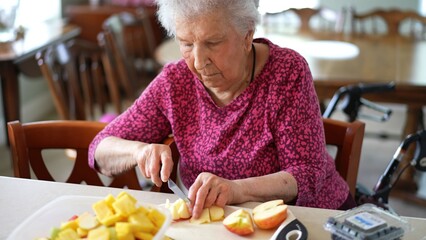 Elderly woman cuts fruit for a salad while sharing the experience with someone on a video call in her kitchen
