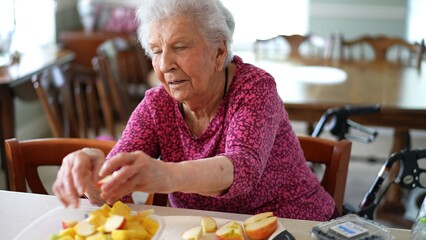 Elderly woman prepares fruit salad using fresh apples and other fruits while communicating through a video call in her kitchen