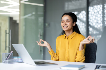 Young businesswoman closing eyes and smiling, practicing meditation in lotus mudra fingers pose at...