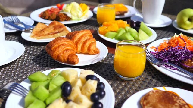 Delicious and healthy breakfast served outdoors in a hotel resort with croissants, pancakes, fresh fruit salad, vegetables, and orange juice on a sunny morning during a summer vacation