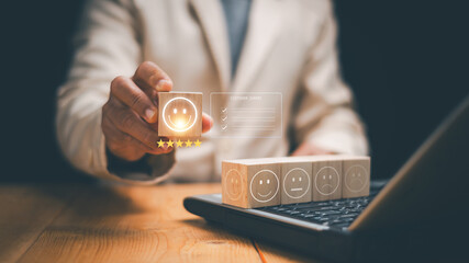 Customer satisfaction concept. Businessman holding smiley face block and five stars above laptop. Service quality, customer experience, online review, survey and business performance evaluation.