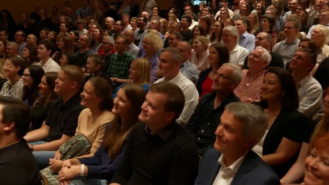 A diverse audience watches a performance in an auditorium, smiling and engaged, enjoying the cultural event.
