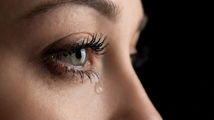 Close-up of a womans eye with a tear rolling down her cheek, expressing sadness and emotion.