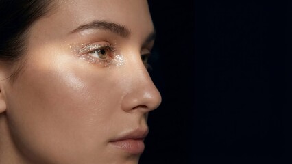 Close-up profile of a womans face with glowing skin against a dark background.