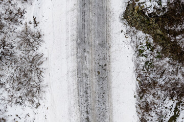Obraz premium Aerial Winter Road Through Snowy Forest Landscape in BC, Canada With Tire Tracks