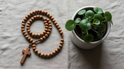 Wooden rosary with cross and green potted plant on textile background. Prayer, faith, and spiritual devotion concept. Christian symbol for worship.