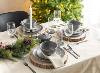 Christmas table setting with candles, plates, and cutlery on a wooden table with a beige...
