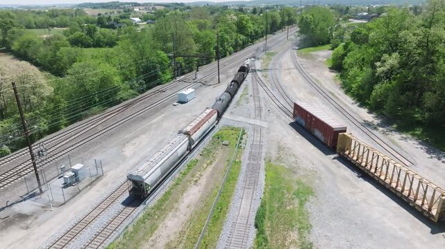 A vintage steam freight train makes its way backing up in yard performing switching operations moving steadily along the railway tracks in a peaceful countryside setting.