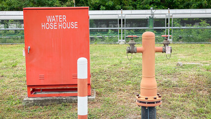 Two fire water supply pipes emerging from the ground with a fire hose cabinet placed alongside, located beside the road,