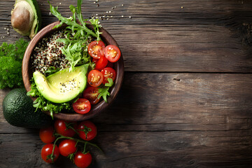 Overhead view of a fresh salad bowl with avocado, cherry tomatoes, and mixed greens on a rustic wooden table.