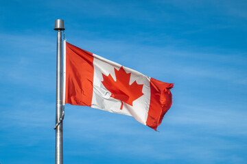 Canadian National Flag Waving on Metal Flagpole Against Clear Blue Sky
