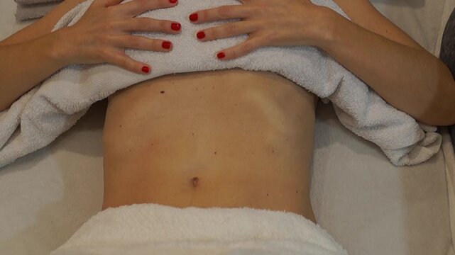 A woman practicing controlled diaphragmatic breathing and gentle abdominal engagement on a massage table to promote relaxation and internal balance.