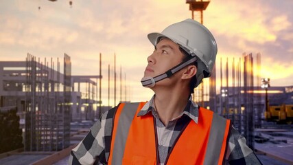 Close Up Of Asian Male Engineer Wearing Safety Helmet Looking Around While Standing With Arms Akimbo at Construction Site with Tower Cranes and Building Foundations