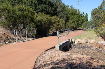 Concrete walking path crossing over a dry creek bed surrounded by trees at the Emerald Botanic Gardens in Queensland, Australia