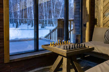 Interior of stylish living room with large window, grey sofa and chessboard on coffee table, winter night