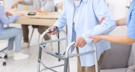 Care worker helping senior woman with walker at retirement home, closeup
