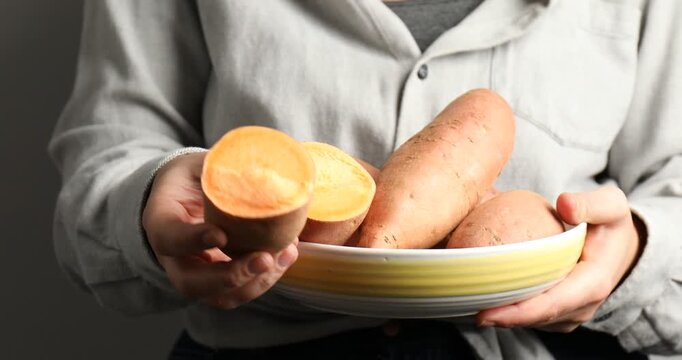 Woman with bowl of raw sweet potatoes on light background, closeup