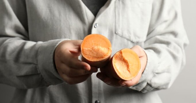 Woman breaking raw sweet potato on light background, closeup