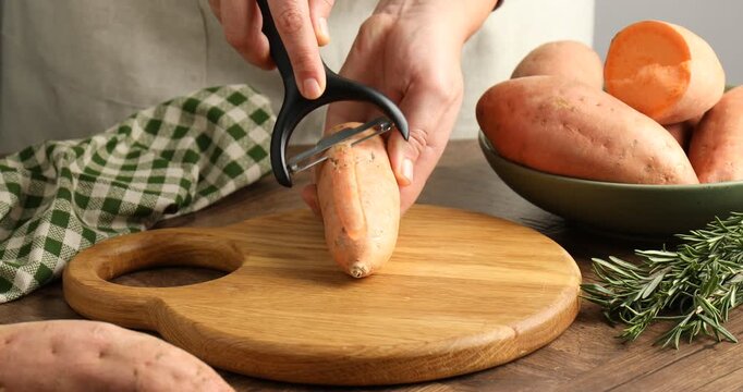 Woman peeling sweet potato at wooden table, closeup