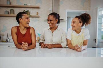 Three generations of happy Black women laughing and bonding together in a modern kitchen at home.